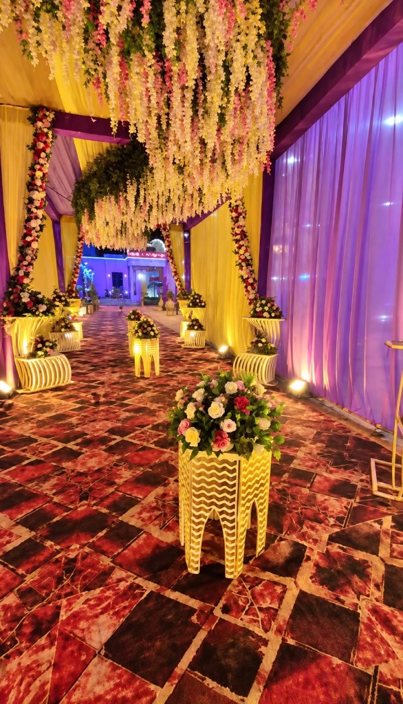 Magical bridal and barat arrival walkway adorned with cascading wisteria flowers, purple silk drapes, and illuminated geometric pedestals